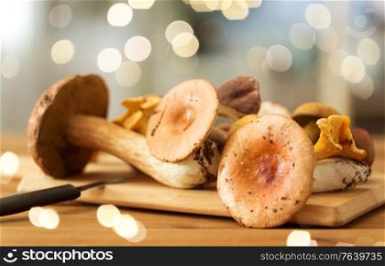 cooking, culinary and edible mushrooms concept - different edible mushrooms and kitchen knife on wooden cutting board. edible mushrooms on wooden cutting board and knife