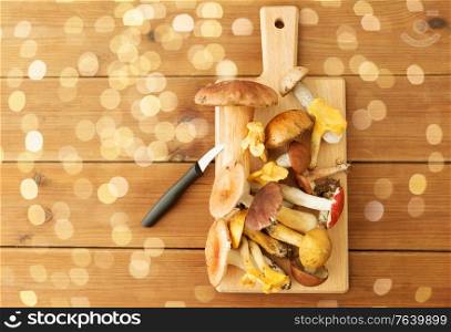 cooking, culinary and edible mushrooms concept - different edible mushrooms and kitchen knife on wooden cutting board. edible mushrooms on wooden cutting board and knife