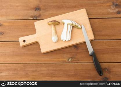 cooking, culinary and edible mushrooms concept - sliced brown cap boletus and kitchen knife on wooden cutting board. edible mushrooms, kitchen knife and cutting board