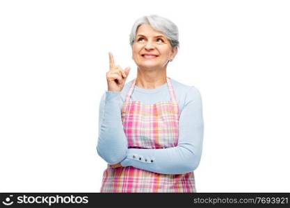 cooking, culinary and old people concept - portrait of smiling senior woman in kitchen apron pointing finger up over white background. smiling senior woman in apron pointing finger up