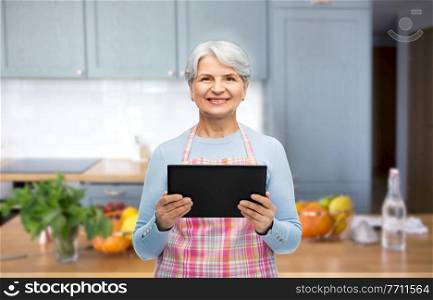 cooking, culinary and old people concept - portrait of smiling senior woman in apron with tablet pc compute over kitchen background. smiling senior woman with tablet pc at kitchen
