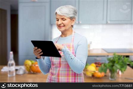 cooking, culinary and old people concept - portrait of smiling senior woman in apron with tablet pc compute over home kitchen background. smiling senior woman in apron with tablet computer