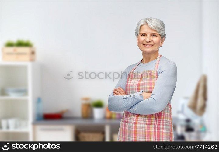 cooking, culinary and old people concept - portrait of smiling senior woman in apron over kitchen background. portrait of smiling senior woman in kitchen apron