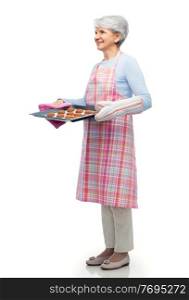 cooking, culinary and old people concept - smiling senior woman in kitchen apron with cookies on baking pan over white background. senior woman in apron with cookies on baking pan