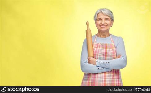 cooking, culinary and old people concept - smiling senior woman in kitchen apron with rolling pin over illuminating yellow background. smiling senior woman in apron with rolling pin