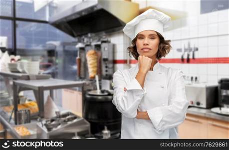 cooking, culinary and people concept - female chef in toque thinking over restaurant or kebab shop kitchen background. female chef in toque thinking at kebab shop