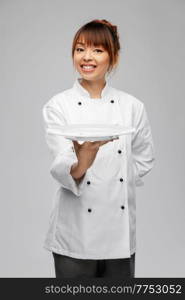 cooking, culinary and people concept - happy smiling female chef holding empty plate over grey background. happy smiling female chef holding empty plate