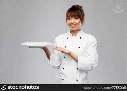 cooking, culinary and people concept - happy smiling female chef holding empty plate over grey background. happy smiling female chef holding empty plate