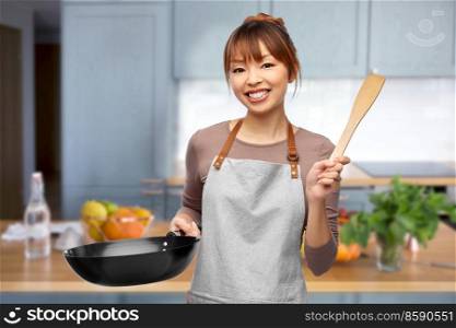 cooking, culinary and people concept - happy smiling female chef in apron with frying pan and spatula over home kitchen background. happy female chef with frying pan in kitchen