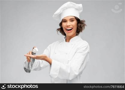 cooking, culinary and people concept - happy smiling female chef in toque with hand sanitizer or liquid soap over grey background. female chef with hand sanitizer or liquid soap