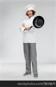 cooking, culinary and people concept - happy smiling female chef in toque with frying pan over grey background. smiling female chef in toque with frying pan