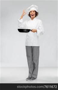 cooking, culinary and people concept - happy smiling female chef in toque with frying pan showing ok hand sign over grey background. smiling female chef with frying pan showing ok