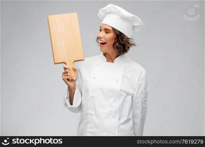 cooking, culinary and people concept - happy smiling female chef in toque with wooden cutting board over grey background. smiling female chef in toque with cutting board