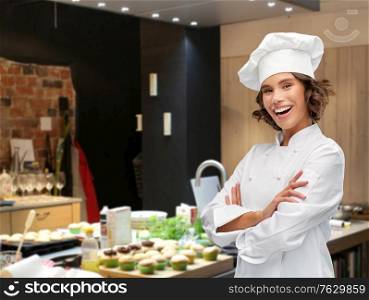 cooking, culinary and people concept - happy smiling female chef in toque with crossed arms over restaurant kitchen background. female chef with crossed arms over restaurant