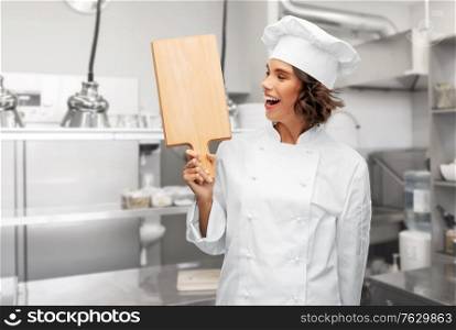 cooking, culinary and people concept - happy smiling female chef in toque with wooden cutting board over restaurant kitchen background. smiling female chef in toque with cutting board