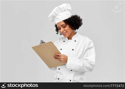 cooking, culinary and people concept - happy smiling female chef in toque and jacket with clipboard over grey background. smiling female chef with clipboard
