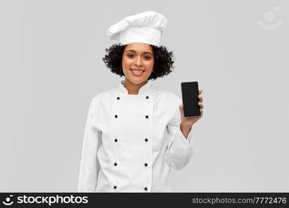 cooking, culinary and people concept - happy smiling female chef in toque and jacket showing smartphone over grey background. smiling female chef showing smartphone