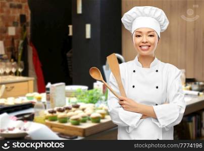 cooking, culinary and people concept - happy smiling female chef in toque with wooden spoon over restaurant kitchen background. happy smiling female chef with wooden spoon