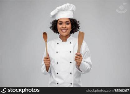 cooking, culinary and people concept - happy smiling female chef in toque with wooden spoon and spatula over grey background. smiling female chef with wooden spoon and spatula