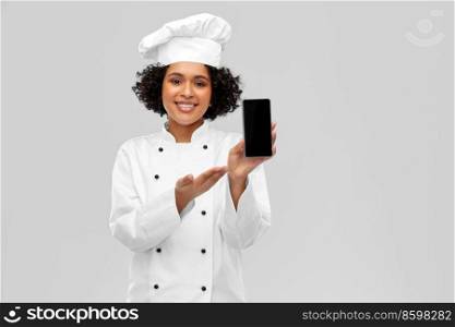 cooking, culinary and people concept - happy smiling female chef in toque and jacket showing smartphone over grey background. smiling female chef showing smartphone