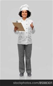 cooking, culinary and people concept - happy smiling female chef in toque and jacket with clipboard showing thumbs up over grey background. female chef with clipboard showing thumbs up