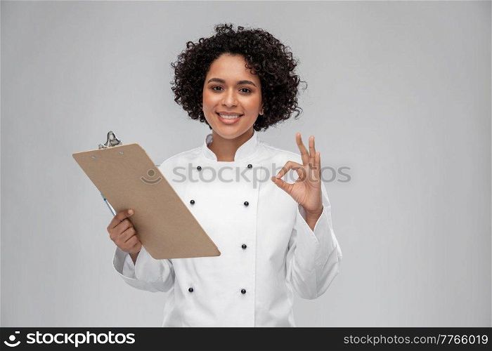 cooking, culinary and people concept - happy smiling female chef in white jacket with clipboard showing ok gesture over grey background. smiling female chef with clipboard