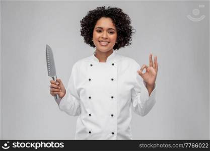 cooking, culinary and people concept - happy smiling female chef in white jacket with kitchen knife showing ok hand sign over grey background. female chef with kitchen knife showing ok sign