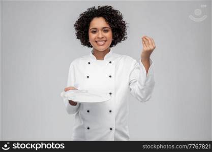cooking, culinary and people concept - happy smiling female chef in white jacket holding empty plate and showing gourmet sign over grey background. happy smiling female chef holding empty plate