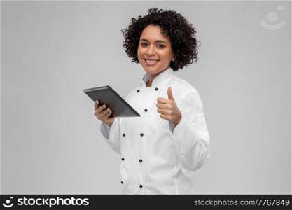 cooking, culinary and people concept - happy smiling female chef in white jacket with tablet pc computer showing thumbs up over grey background. happy female chef with tablet pc showing thumbs up
