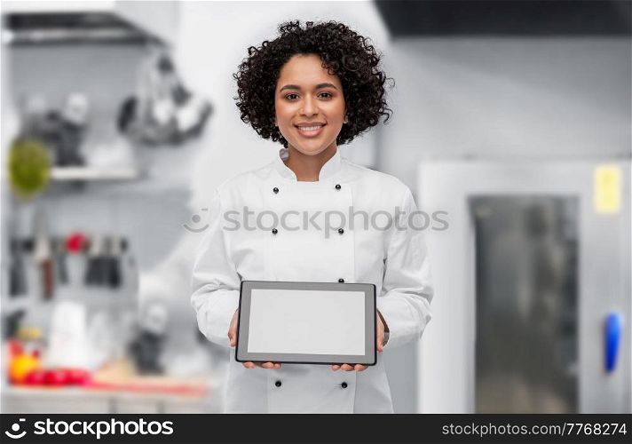 cooking, culinary and people concept - happy smiling female chef in white jacket showing tablet pc computer over restaurant kitchen background. smiling female chef showing tablet pc on kitchen