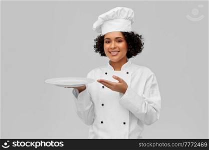 cooking, culinary and people concept - happy smiling female chef in white toque and jacket holding empty plate over grey background. happy smiling female chef holding empty plate