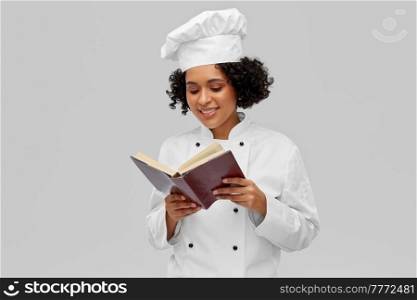 cooking, culinary and people concept - happy smiling female chef in white toque and jacket reading cook book over grey background. happy female chef in white toque reading cook book