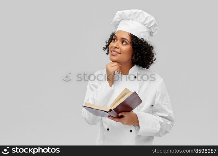 cooking, culinary and people concept - happy smiling female chef in white toque and jacket reading cook book over grey background. happy female chef in white toque reading cook book