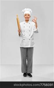 cooking, culinary and people concept - happy smiling female chef or baker with rolling pin showing ok gesture over grey background. smiling female chef or baker with rolling pin