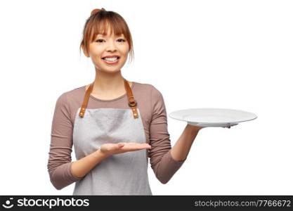 cooking, culinary and people concept - happy smiling female chef or waitress in apron with empty plate over white background. happy woman in apron with empty plate