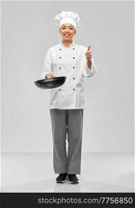 cooking, culinary and people concept - happy smiling female chef with frying pan showing thumbs up gesture over grey background. female chef with frying pan showing thumbs up