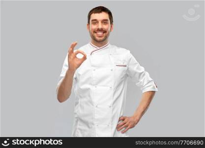 cooking, culinary and people concept - happy smiling male chef in jacket showing ok hand sign over grey background. happy smiling male chef showing ok hand sign