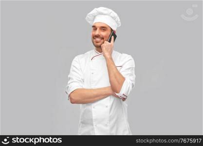 cooking, culinary and people concept - happy smiling male chef in toque and jacket calling on smartphone over grey background. happy smiling male chef calling on smartphone