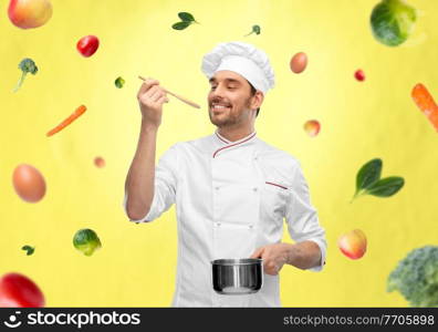 cooking, culinary and people concept - happy smiling male chef in toque with pot or saucepan and spoon tasting food over vegetables on illuminating yellow background. happy smiling male chef with saucepan tasting food