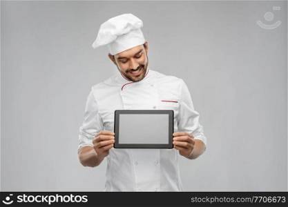 cooking, culinary and people concept - happy smiling male chef in toque showing tablet pc computer over grey background. happy smiling male chef showing tablet pc computer