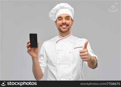 cooking, culinary and people concept - happy smiling male chef in toque showing smartphone and thumbs up over grey background. happy chef with smartphone showing and thumbs up