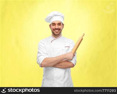 cooking, culinary and people concept - happy smiling male chef or baker in toque with rolling pin over illuminating yellow background. happy smiling male chef or baker with rolling pin