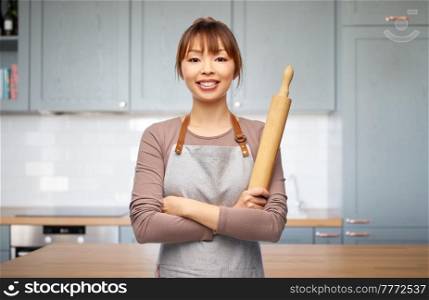 cooking, culinary and people concept - happy smiling woman in apron with wooden rolling pin over kitchen background. happy woman in apron with wooden rolling pin