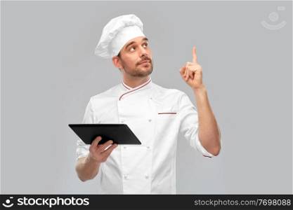 cooking, culinary and people concept - male chef in toque with tablet pc computer pointing finger up over grey background. male chef with tablet computer pointing finger up