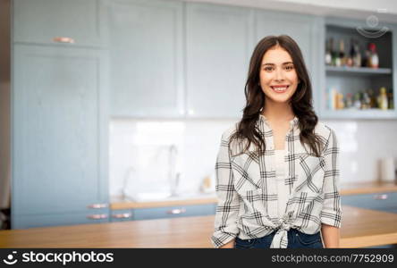 cooking, culinary and people concept - smiling young woman or teenage girl in checkered shirt at home over kitchen background. young woman or teenage girl at kitchen