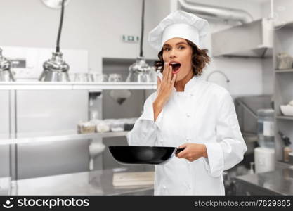 cooking, culinary and people concept - surprised female chef in toque with frying pan over restaurant kitchen background. surprised female chef in toque with frying pan