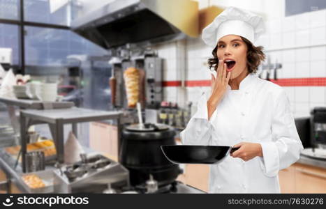 cooking, culinary and people concept - surprised female chef in toque with frying pan over restaurant or kebab shop kitchen background. surprised chef with frying pan at kebab shop