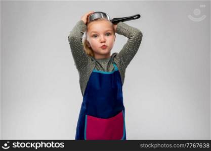 cooking, culinary and profession concept - happy little girl in apron playing with saucepan over grey background. happy little girl in apron playing with saucepan
