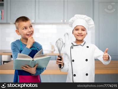 cooking, culinary and profession concept - happy smiling little boy and girl with cook book and whisk over kitchen background. children with cook book and whisk in kitchen