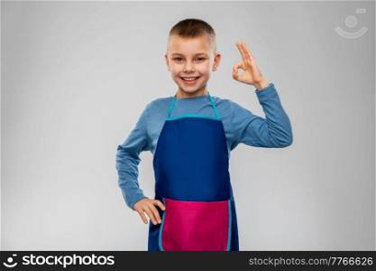 cooking, culinary and profession concept - happy smiling little boy in apron showing ok gesture over grey background. smiling little boy in apron